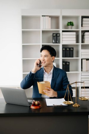 Photo for Asian male lawyer chatting online with client on smartphone, discussing details of lawsuit in modern office - Royalty Free Image