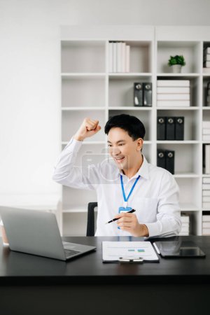 Photo for Happy Asian businessman feeling excited about his professional success. Young man making winner's gesture in office - Royalty Free Image