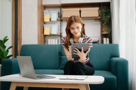 Photo for Female student sitting at sofa using tablet computer to search an online informations in living room - Royalty Free Image