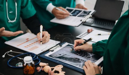Photo for Medical team having a meeting with doctors in white lab coats and surgical scrubs seated at table discussing  patients working online using computers in the medical industry - Royalty Free Image