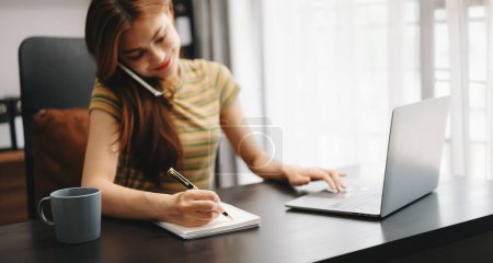 Photo for Businesswoman hand working with laptop computer and making notes in notepad - Royalty Free Image