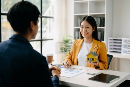 Téléchargez les photos : Femme agent immobilier asiatique présentant un projet d'investissement et parlant de nouvelle maison à un client masculin - en image libre de droit