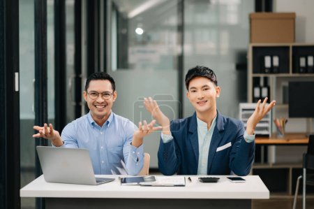 Téléchargez les photos : Deux hommes d'affaires asiatiques souriant assis ensemble dans un bureau moderne - en image libre de droit