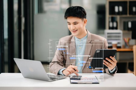Photo for Businessman updating tasks using Gantt chart scheduling virtual diagram. Young Asian man working with laptop in modern office - Royalty Free Image