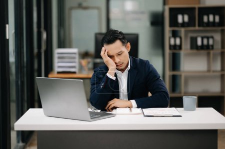 Photo for Overworked young Asian businessman feeling tired after a long day at work. Office syndrome - Royalty Free Image