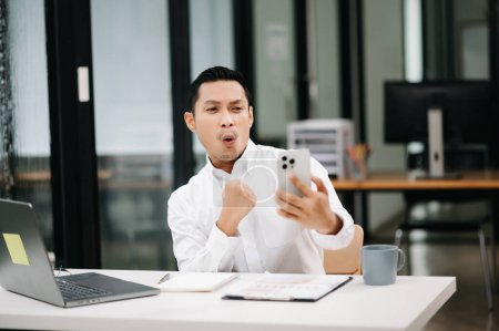 Téléchargez les photos : Asiatique homme d'affaires se sentant heureux avec ses réalisations commerciales dans le bureau moderne. - en image libre de droit