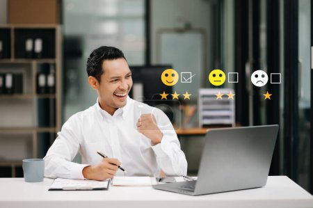 Foto de Concepto de evaluación del servicio al cliente. Asiático hombre de negocios presionando cara sonrisa emoticono en la pantalla virtual en la oficina - Imagen libre de derechos