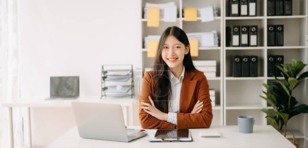 Téléchargez les photos : Jeune femme asiatique attrayante souriant et travaillant de la maison, regardant la caméra au bureau moderne - en image libre de droit