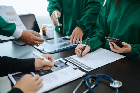 Téléchargez les photos : Équipe médicale en réunion avec des médecins en blouse blanche et en gommage chirurgical assis à table pour discuter d'un patient travaillant en ligne à l'aide d'ordinateurs dans l'industrie médicale - en image libre de droit
