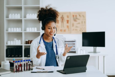 Photo for Attractive African female doctor explaining medical treatment to patient through a video call with laptop in office - Royalty Free Image