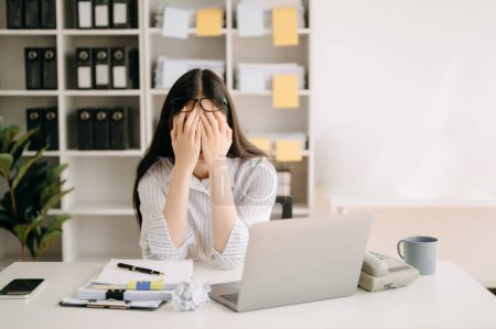 Asiatin spürt Migräne-Kopfschmerzen. Überarbeitete Unternehmerin arbeitet im Büro am Laptop