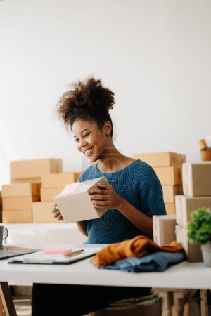 Photo for Startup small business SME, African woman entrepreneur checking online orders and preparing parcels for shipping - Royalty Free Image
