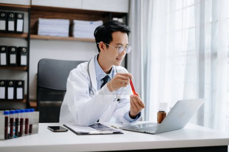 Téléchargez les photos : Médecin attrayant parlant tout en expliquant le traitement médical au patient par un appel vidéo avec ordinateur portable dans le bureau - en image libre de droit