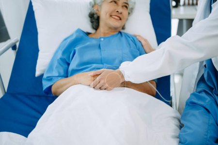 Téléchargez les photos : Médecin femme tenant la main du patient aîné sur le lit avec une solution saline à l'hôpital ou à la clinique - en image libre de droit