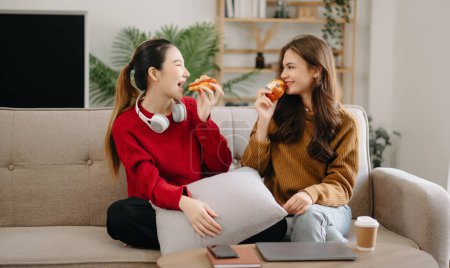Photo for Two asian beauty smiling young women sitting on sofa, having fun watch comedy video on TV in house. Activity lifestyle concept in living room - Royalty Free Image