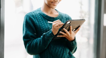 Téléchargez les photos : Belle femme africaine tenant et utilisant une tablette numérique au bureau à domicile - en image libre de droit