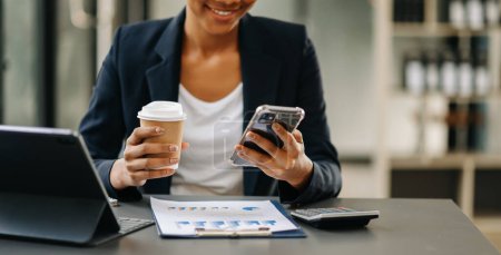 Téléchargez les photos : Femme d'affaires utilisant un téléphone intelligent et boire du café au bureau - en image libre de droit