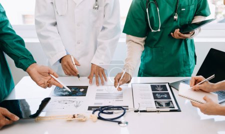 Téléchargez les photos : Équipe médicale en réunion avec des médecins en blouse blanche et en gommage chirurgical assis à une table pour discuter d'un patient travaillant en ligne à l'aide d'ordinateurs dans l'industrie médicale - en image libre de droit