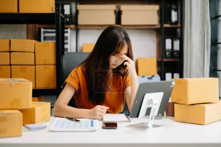 Photo for Startup small business SME, tired Asian woman entrepreneur checking online orders and preparing parcels for shipping - Royalty Free Image