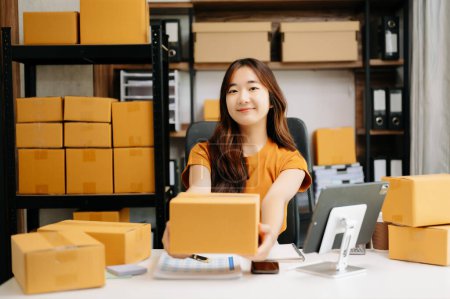 Téléchargez les photos : Petite entreprise en démarrage PME, femme entrepreneur asiatique vérifiant les commandes en ligne et préparant des colis pour l'expédition - en image libre de droit