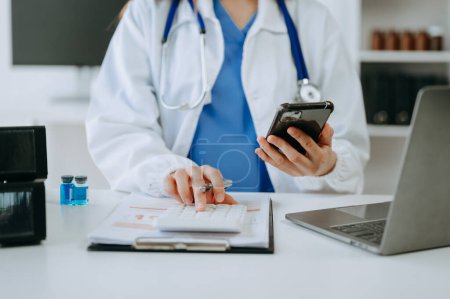 Photo for Healthcare costs and fees concept. Doctor using calculator and smartphone in his office - Royalty Free Image