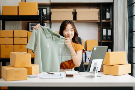 Foto de Concepto de blogger de moda, Mujer joven asiática vendiendo ropa en streaming de video. Puesta en marcha de pequeñas empresas PYME - Imagen libre de derechos