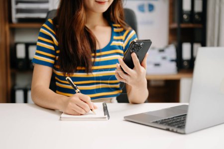 Foto de Mujer de negocios trabajando a mano con ordenador portátil y tomando notas en bloc de notas - Imagen libre de derechos