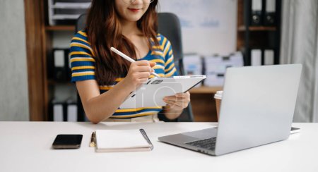 Téléchargez les photos : Femme d'affaires main de travail avec ordinateur portable et de prendre des notes dans le bloc-notes - en image libre de droit