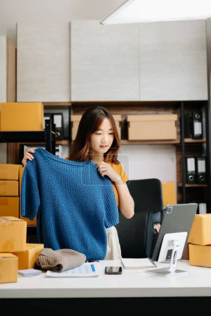 Foto de Concepto de blogger de moda, Mujer joven asiática vendiendo ropa en streaming de video. Puesta en marcha de pequeñas empresas PYME - Imagen libre de derechos