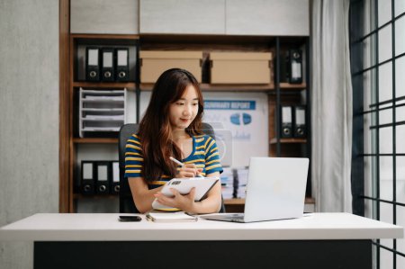 Foto de Joven asiática confiada con una sonrisa trabajando en la tableta digital en la oficina moderna. - Imagen libre de derechos