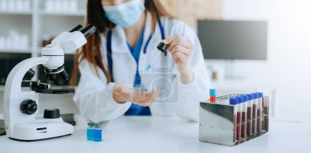 Téléchargez les photos : Médecin féminin travaillant au microscope et aux éprouvettes en laboratoire - en image libre de droit