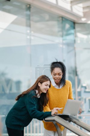 Foto de Las mujeres de negocios que van en el centro de la ciudad en el estilo de negocios casual inteligente, hablando, trabajando juntos en el ordenador portátil - Imagen libre de derechos