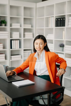 Foto de Joven atractivo asiático mujer oficina trabajador traje de trabajo con bloc de notas y portátil en la oficina moderna - Imagen libre de derechos