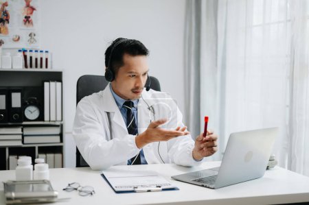 Téléchargez les photos : Médecin masculin attrayant expliquant le traitement médical au patient par un appel vidéo dans son bureau - en image libre de droit