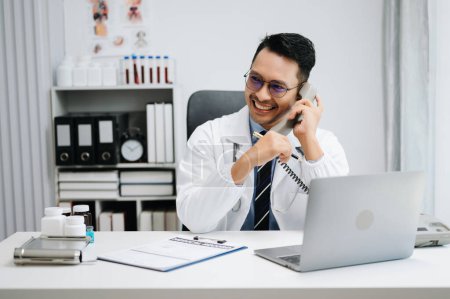 Téléchargez les photos : Heureux médecin masculin parlant au téléphone au bureau - en image libre de droit