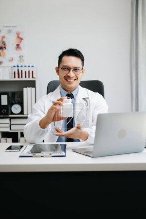Téléchargez les photos : Médecin masculin attrayant expliquant le traitement médical au patient par un appel vidéo dans son bureau - en image libre de droit