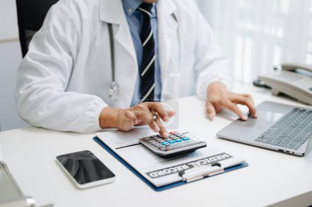 Foto de Concepto de costos y tarifas de atención médica. Doctor usando calculadora y teléfono inteligente en su oficina - Imagen libre de derechos