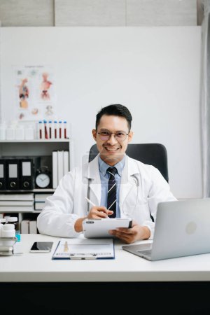 Foto de Confiado joven doctor masculino en uniforme médico blanco que trabaja en la computadora - Imagen libre de derechos