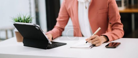 Téléchargez les photos : Femme d'affaires travaillant avec un nouvel ordinateur moderne et prenant des notes dans le bureau - en image libre de droit