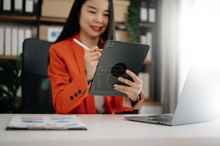 Téléchargez les photos : Femme asiatique confiante avec tablette numérique et ordinateur portable travaillant dans le bureau. - en image libre de droit