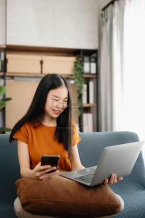 Téléchargez les photos : Asiatique fille dans la bibliothèque assis sur le canapé en utilisant un ordinateur portable pour rechercher des informations en ligne - en image libre de droit