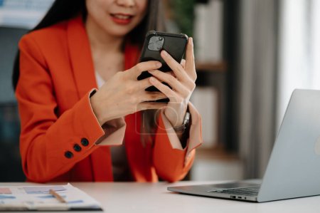 Téléchargez les photos : Femme asiatique confiante avec smartphone et ordinateur portable travaillant dans le bureau. - en image libre de droit