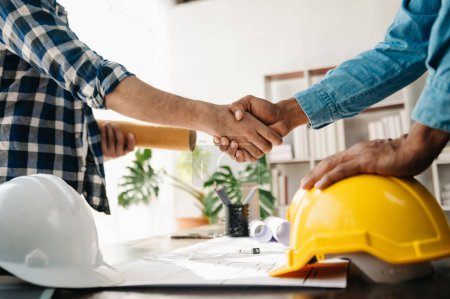 Photo for Construction team shake hands, greeting start new project plan behind yellow helmet on desk in office center to consults about their building project. - Royalty Free Image