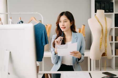 Téléchargez les photos : Femme tailleur asiatique travaillant avec des vêtements dans un atelier de couture. Belle jeune créatrice de mode en studio - en image libre de droit