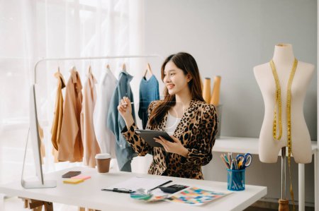 Téléchargez les photos : Femme tailleur asiatique travaillant avec des vêtements dans un atelier de couture. Belle jeune créatrice de mode en studio - en image libre de droit