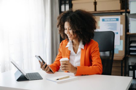 Téléchargez les photos : Jeune belle femme utilisant un smartphone et une tablette tout en étant assis à la table de travail en bois bureau moderne - en image libre de droit