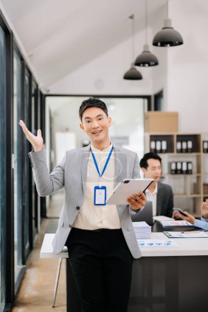Téléchargez les photos : Jeune asiatique attrayant employé de bureau en costumes d'affaires souriant à la caméra dans le bureau moderne - en image libre de droit