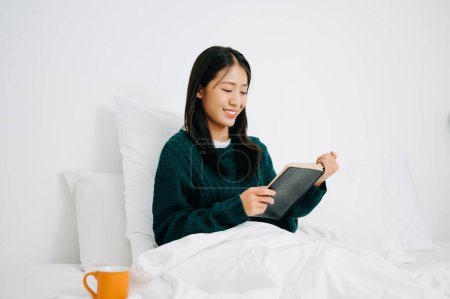 Téléchargez les photos : Portrait de jeune femme lisant le livre et se reposant au lit dans la chambre le matin, concept de style de vie - en image libre de droit