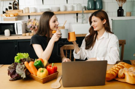 Téléchargez les photos : Deux étudiants asiatiques apprenant en ligne ensemble sur ordinateur portable dans la cuisine ou le salon à la maison. - en image libre de droit