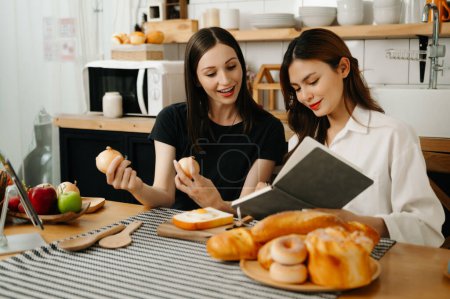 Foto de Dos hermosas mujeres en la cocina en un delantal, verduras frescas sobre la mesa, escribe sus recetas favoritas, se le ocurren ideas para los platos - Imagen libre de derechos